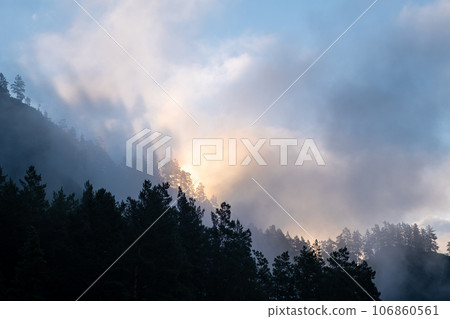 Mountains and peaks in fog at sunrise or sunset. Sun from behind the mountain. Amazing view of mountains and forest landscape with cloudy skies Altai mountains. Mountains and peaks in fog at sunrise Mountains and peaks in fog at sunrise or sunset. Sun from behind the mountain. Amazing view of mountains and forest landscape with cloudy skies Altai mountains. Mountains and peaks in fog at sunrise 106860561