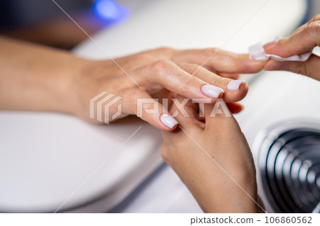 Nail care procedure in a beauty salon. Female hands and tools for manicure, process of performing manicure in beauty salon. Concept spa body care. Gloved hands of a skilled manicurist cutting cuticles 106860562