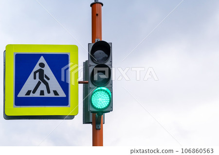 A pedestrian crossing sign with a reflective coating and a traffic light is installed on the street next to the school and warns drivers about the pedestrian crossing. Be careful on the road 106860563