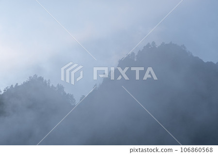 Mountains and peaks in fog at sunrise or sunset. Sun from behind the mountain. Amazing view of mountains and forest landscape with cloudy skies Altai mountains. Mountains and peaks in fog at sunrise 106860568