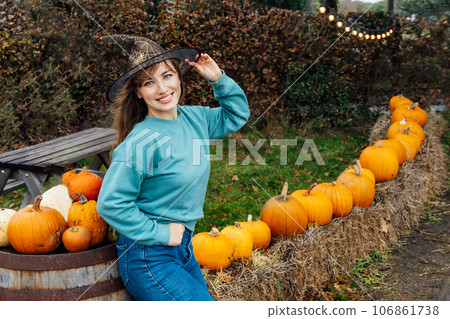 Portrait of smiling young woman in witch hat posing on pumpkins background. Female selecting best pumpkins for Thanksgiving and Halloween holidays decor on agriculture farm. Autumn fall festive mood. 106861738