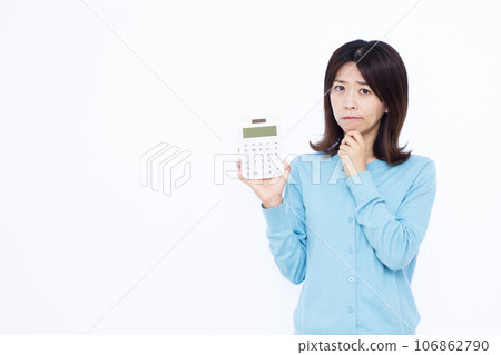 A housewife in her 30s holding a calculator and worrying in front of a white background A housewife in her 30s holding a calculator and worrying in front of a white background 106862790