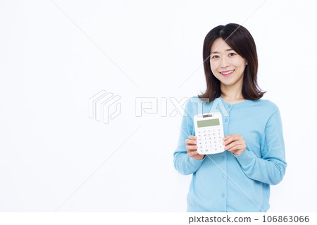 A housewife in her 30s holding a calculator in front of a white background A housewife in her 30s holding a calculator in front of a white background 106863066