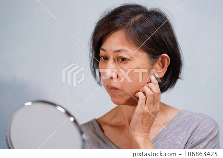 一位中年婦女,面容蒼老,臉頰上有皺紋和斑點 一位中年婦女,面容蒼老,臉頰上有皺紋和斑點 106863425