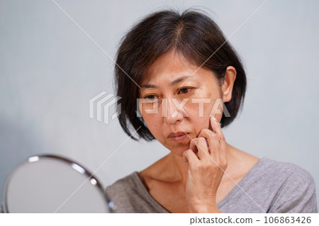 A middle-aged woman with an aging face and wrinkles and spots on her cheeks A middle-aged woman with an aging face and wrinkles and spots on her cheeks 106863426