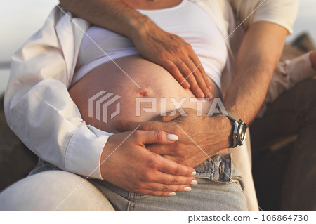 unrecognizable body of pregnant woman in casual and hands of parents intertwined on stomach 106864730