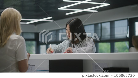 Female administrator consults Asian woman, helps fill out papers in hospital 106865720