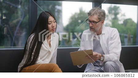 Doctor talks with Asian woman in clinic waiting room Doctor talks with Asian woman in clinic waiting room 106865812