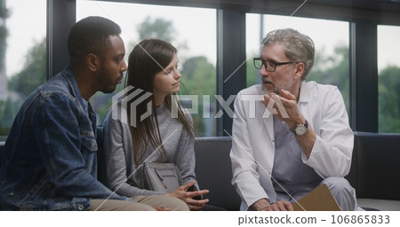 Doctor talks with multiethnic couple in clinic lobby area 106865833