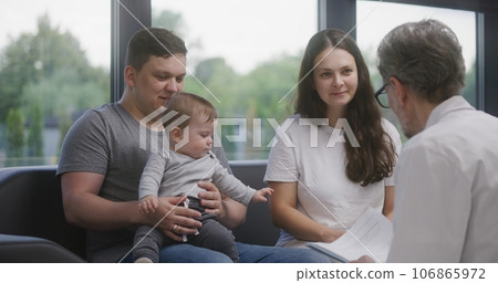Family with little child sit on couch, speak with doctor 106865972