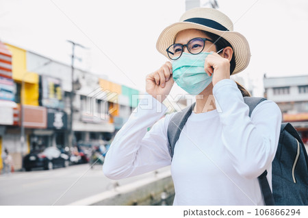 Asian woman wearing mask while travel during the COVID-19 Pandemic. During your trip should wear a mask to keep your nose and mouth covered when in public. 106866294