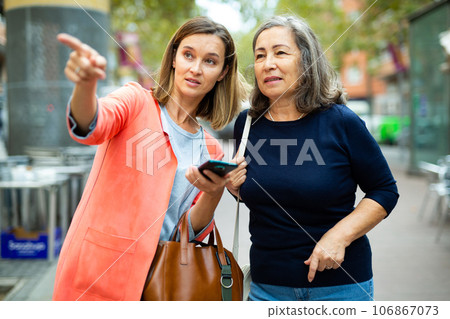 Friendly girl helping elderly woman to necessary address in city 106867073