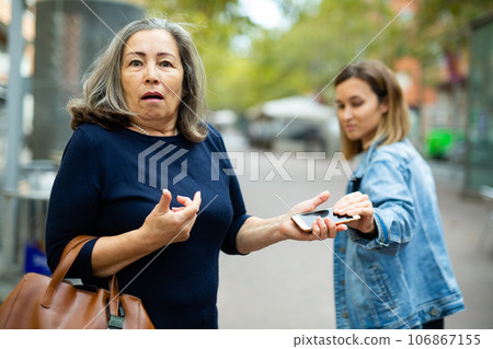 Female thief trying to snatch phone of elderly woman outdoors Female thief trying to snatch phone of elderly woman outdoors 106867155