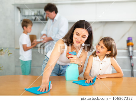 Friendly family tidy up room together. Mom and daughter are dusting the table. Father and son vacuuming room 106867352