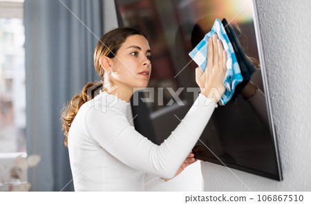 Young woman householder using rag to wash TV display Young woman householder using rag to wash TV display 106867510