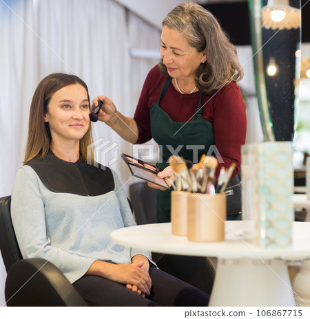 Elderly female makeup artist applying blush to woman face 106867715