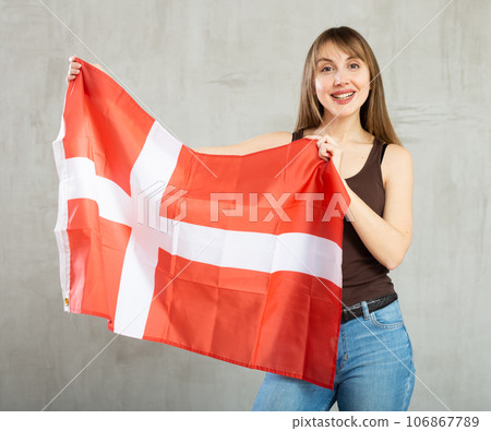 Happy young woman holding flag of Denmark against unicoloured background 106867789