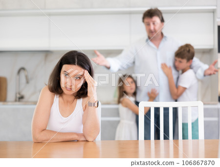 Adult woman sitting at table quarreling with family Adult woman sitting at table quarreling with family 106867870