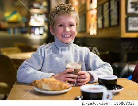 Happy preteen boy enjoying hot chocolate with croissant in cafe 106868025