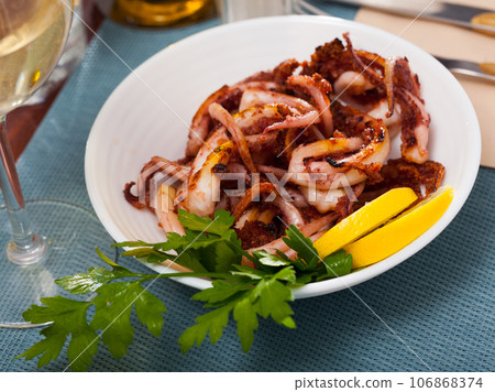 Delicious cooked squid or octopus tentacles with lemon and parsley on a plate 106868374