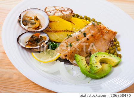 Fried trout fillets served with vegetables, seashells and avocado at plate 106868470
