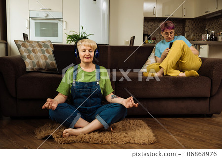 Mature caucasian woman meditating through headphones at home Mature caucasian woman meditating through headphones at home 106868976