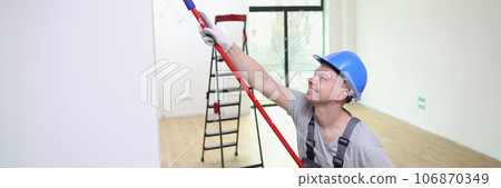 Happy decorator paints house wall with roller brush and white paint. Happy decorator paints house wall with roller brush and white paint. 106870349