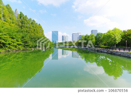 Trees and buildings reflected in the water surface of Osaka Castle's moat 2023-08-21 106870556