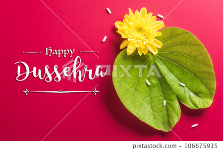 Happy Dussehra. Yellow flowers, green leaf, rice and the text on red paper background. Dussehra Indian Festival concept. Happy Dussehra. Yellow flowers, green leaf, rice and the text on red paper background. Dussehra Indian Festival concept. 106875915