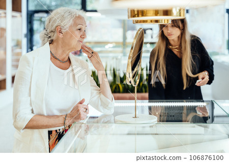 Happy stylish mature old woman pensioner admiring his reflection in the mirror in jewelry store. 106876100