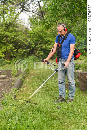 Man mowing tall grass. Process of lawn trimming with hand mower. 106876633