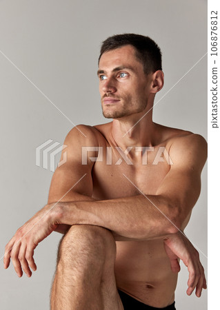 Portrait of handsome young man with grey eyes, posing shirtless against grey studio background. Muscular body Portrait of handsome young man with grey eyes, posing shirtless against grey studio background. Muscular body 106876812