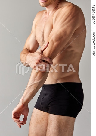 Hand pain, sprain. Cropped image of muscular man with relief body in underwear holding elbow against grey studio background 106876838