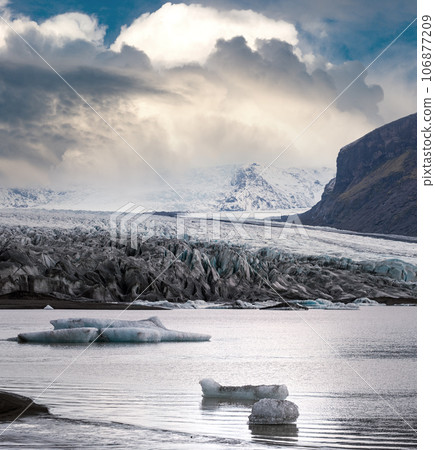 Skaftafellsjokull glacier, Iceland. Glacier tongue slides from the Vatnajokull icecap or Vatna Glacier near subglacial Esjufjoll volcano. Glacial lagoon with blocks of ice and surrounding mountains. Skaftafellsjokull glacier, Iceland. Glacier tongue slides from the Vatnajokull icecap or Vatna Glacier near subglacial Esjufjoll volcano. Glacial lagoon with blocks of ice and surrounding mountains. 106877209