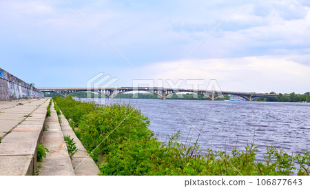 Stone river embankment overgrown with green bushes, metro bridge Stone river embankment overgrown with green bushes, metro bridge 106877643