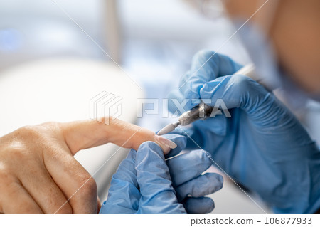 Nail care procedure in a beauty salon. Female hands and tools for manicure, process of performing manicure in beauty salon. Concept spa body care. Gloved hands of a skilled manicurist cutting cuticles Nail care procedure in a beauty salon. Female hands and tools for manicure, process of performing manicure in beauty salon. Concept spa body care. Gloved hands of a skilled manicurist cutting cuticles 106877933