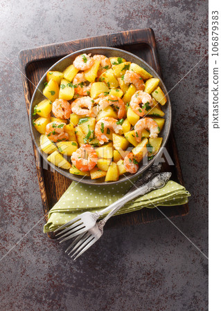 Homemade fried potatoes with garlic, herbs and shrimp close-up in a plate. Vertical top view 106879383