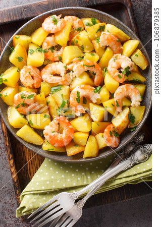 Mediterranean cuisine fried potatoes with shrimp, parsley and garlic close-up in a plate on the table. Vertical top view 106879385