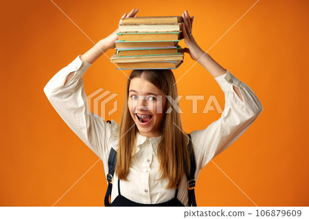 Teen schoolgirl holding stack of books over head on yellow background Teen schoolgirl holding stack of books over head on yellow background 106879609