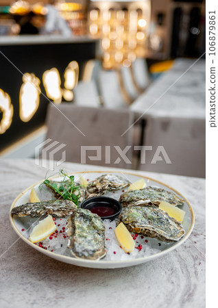 Plate with oysters on ice and sauce on a marble table Plate with oysters on ice and sauce on a marble table 106879861