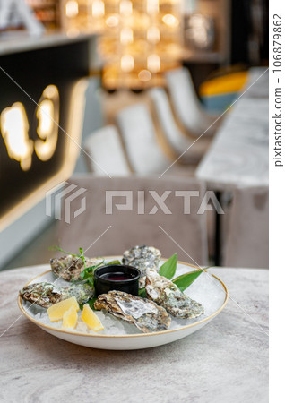 Plate with oysters on ice and sauce on a marble table Plate with oysters on ice and sauce on a marble table 106879862