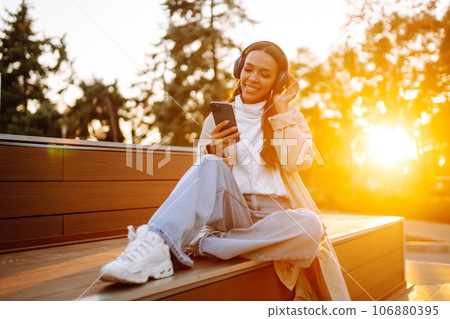 Young woman in headphones listening music, chatting outdoors. Lifestyle, relax, technology concept. 106880395