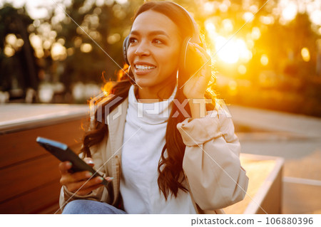 Young woman in headphones listening music, chatting outdoors. Lifestyle, relax, technology concept. 106880396