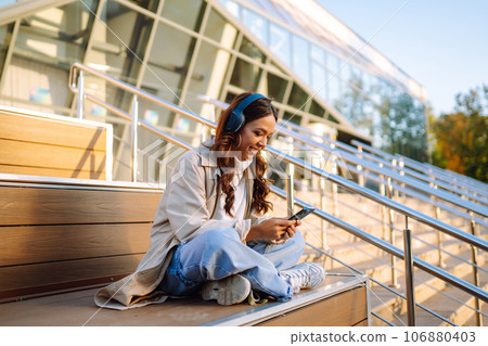 Young woman listening to music with headphones outdoors. The concept of people, music, emotions. 106880403