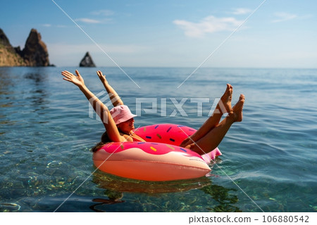 Summer vacation woman in hat floats on an inflatable donut mattress. Happy woman relaxing and enjoying family summer travel holidays travel on the sea. Summer vacation woman in hat floats on an inflatable donut mattress. Happy woman relaxing and enjoying family summer travel holidays travel on the sea. 106880542