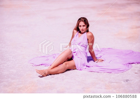 A woman in a pink dress sits on the salty shore of a pink lake and poses for a souvenir photo, creating lasting memories. A woman in a pink dress sits on the salty shore of a pink lake and poses for a souvenir photo, creating lasting memories. 106880588