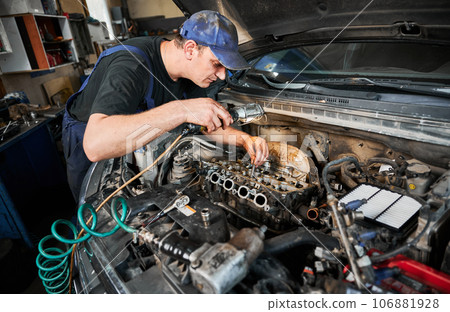 Man worker fixing car engine, working in garage, workshop, servicing center. Repairman, mechanic opening hood of car, examining. Man worker fixing car engine, working in garage, workshop, servicing center. Repairman, mechanic opening hood of car, examining. 106881928
