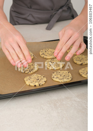 teenager boy's hands put raw american chocolate chip cookies on baking sheet. vertical shot of young chef hands making cookies 106883467