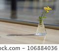 Yellow flowers in a small glass vase by the window 106884036