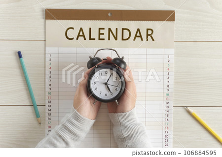 Girl's hand holding a clock on the calendar. Appointments, schedules, plans, reservations, etc. 106884595